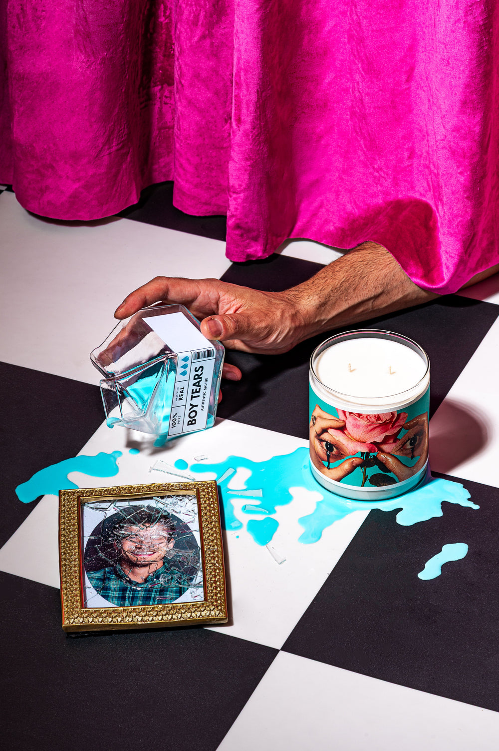 Person holding a small glass container next to a candle with a floral design on a checkered surface.