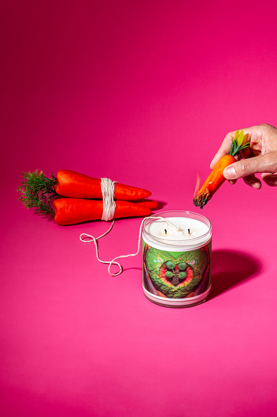 Candle with a decorative design on a pink background, surrounded by carrots.